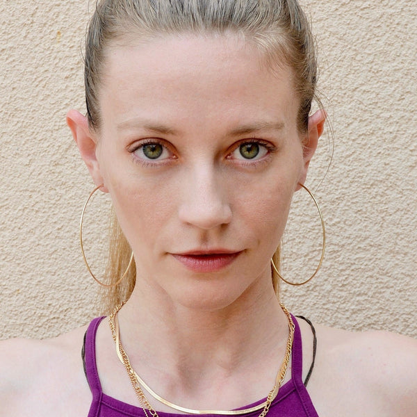 front facing photo of blond green-eyed woman wearing large thin gold hoops and a purple top